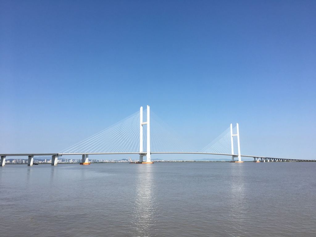 Podul rutier cu cabluri peste fluviul Yalu, între China și Coreea de Nord, sub cerul senin, cu stâlpi albi.