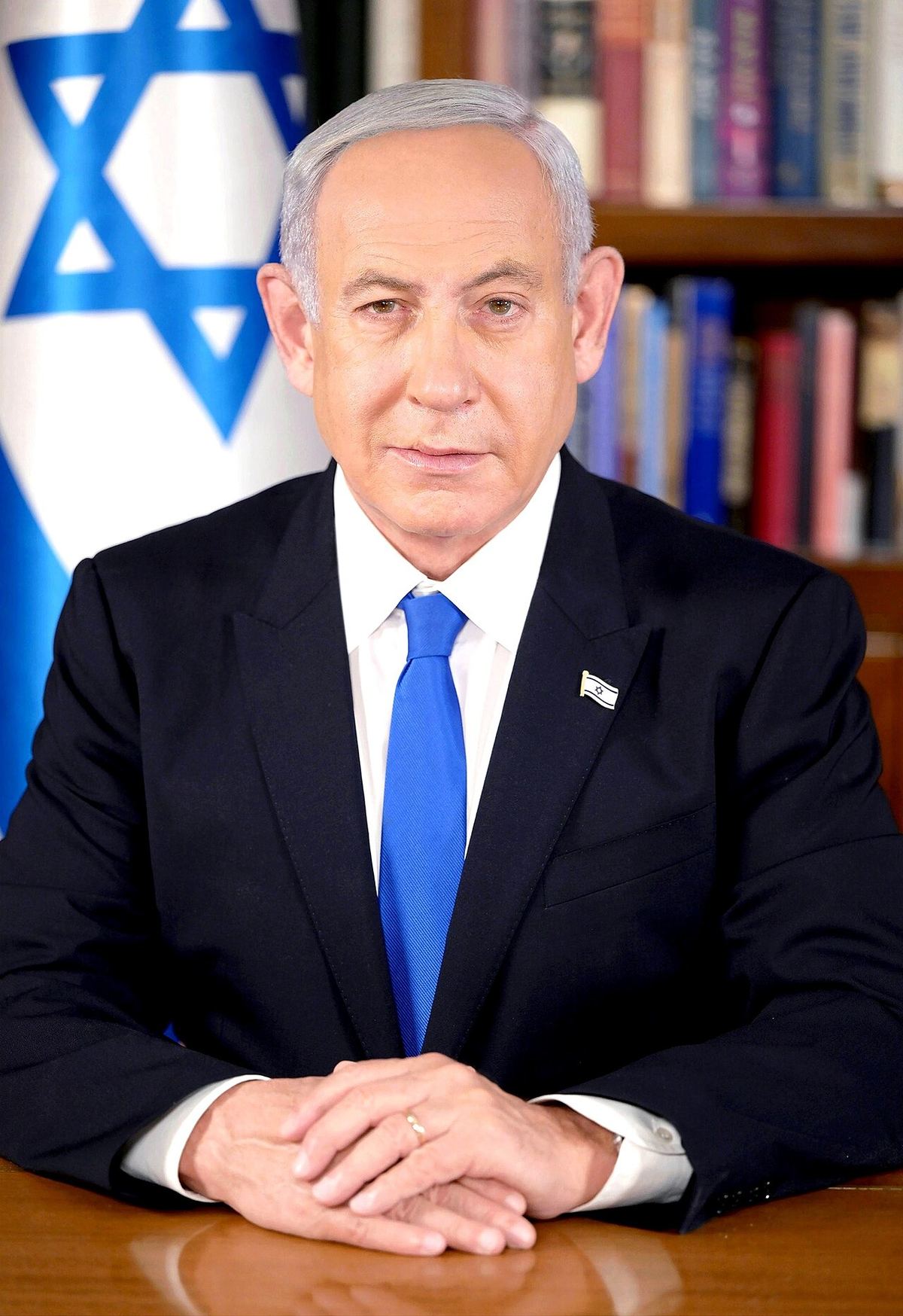 Portretul premierului israelian Benjamin Netanyahu, în costum bleumarin și cravată albastră, în fața steagului Israelului.