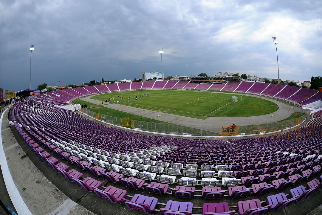 Vedere panoramică a stadionului Dan Păltinișanu din Timișoara, cu tribunele goale și terenul de fotbal verde (fotografie de arhivă).