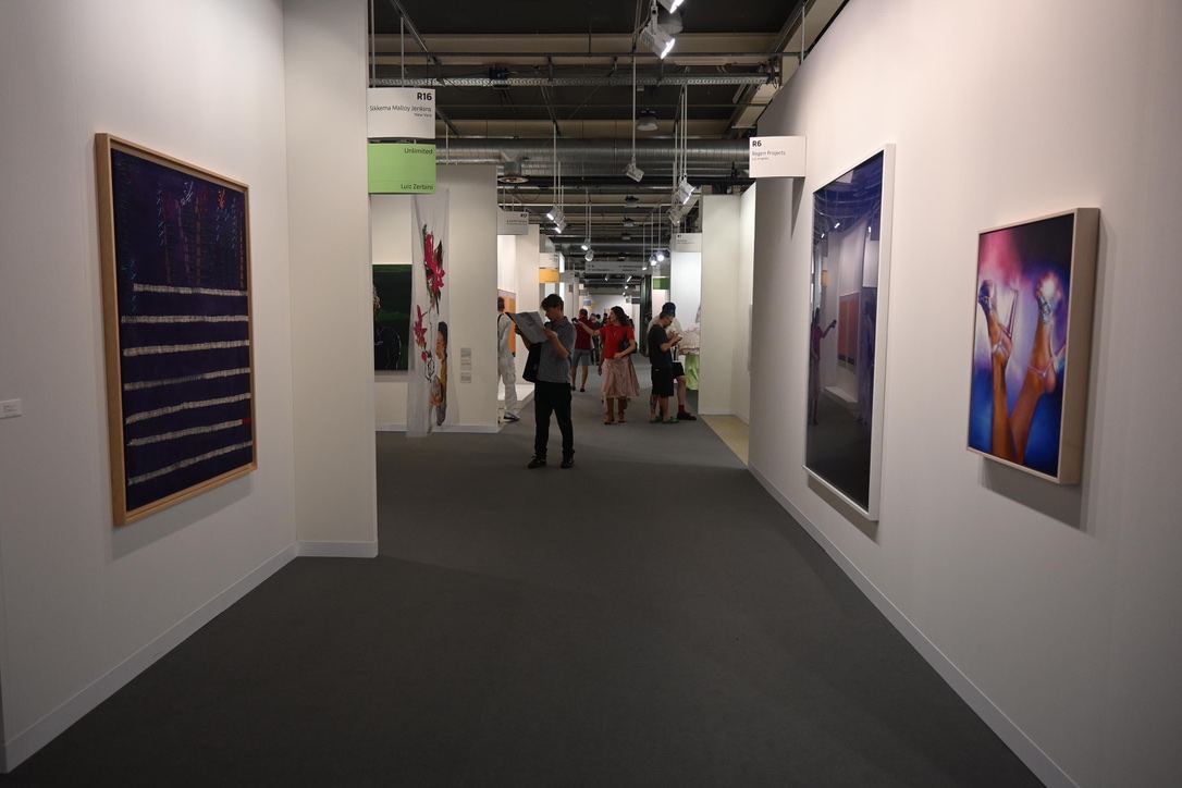 Interior de galerie de artă cu tablouri expuse pe pereți și vizitatori, la Art Basel 2025 din Elveția.