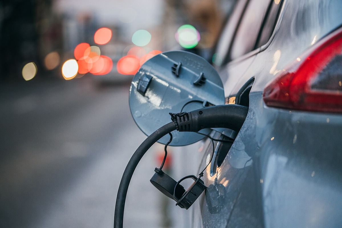Un cablu de încărcare conectat la o mașină electrică, pe o stradă urbană cu lumini de circulație neclare în fundal.