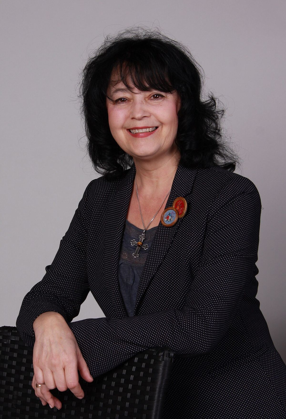 Portretul cântăreței Minodora, într-un sacou negru cu buline, zâmbind, așezată lângă un scaun din ratan.