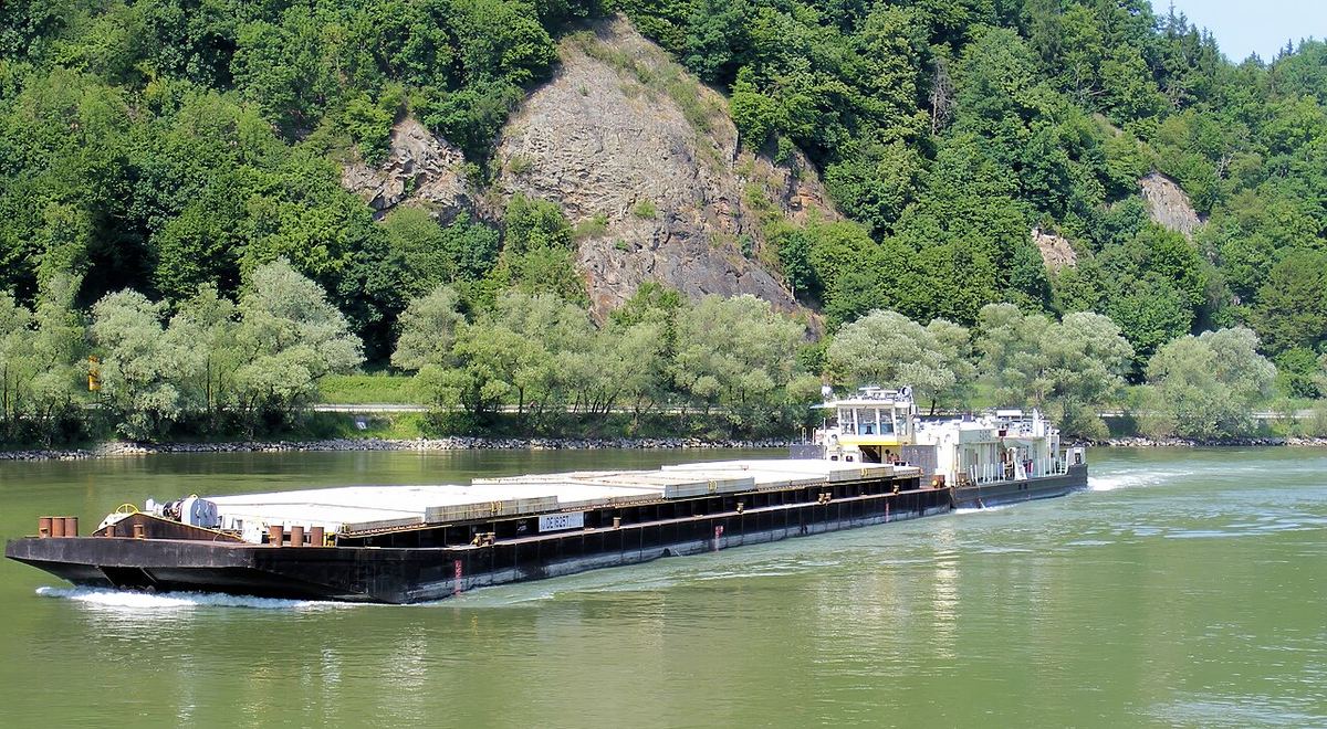 Remorcher fluvial împingând o barjă pe un râu, imagine ilustrativă a transportului fluvial.