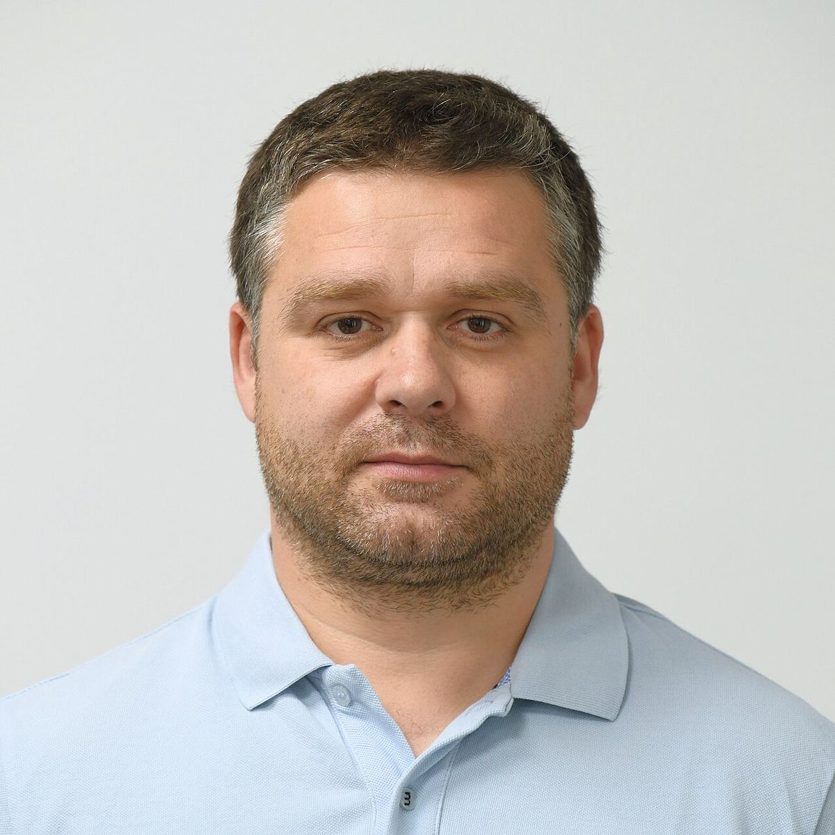 Portretul primarului general Ciprian Ciucu, într-o cămașă polo albastru deschis, pe un fundal gri neutru.