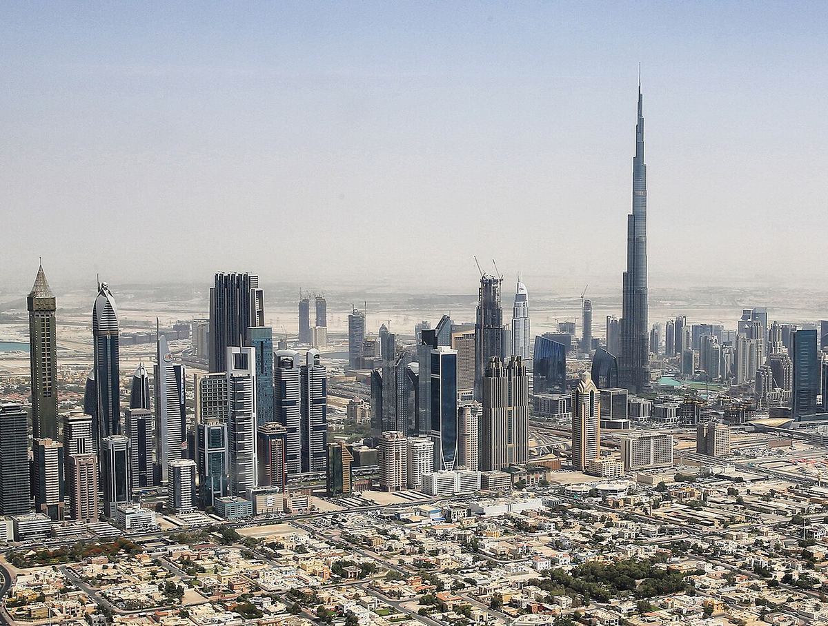 Vedere aeriană a skyline-ului din centrul Dubaiului, cu turnul Burj Khalifa în dreapta, printre zgârie-nori și clădiri rezidențiale.