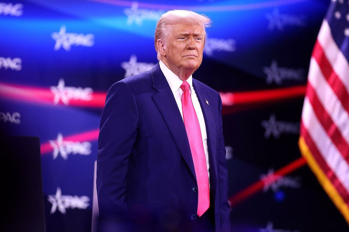 Donald Trump în fața unui decor CPAC albastru, cu un steag american în dreapta, într-o fotografie de arhivă.