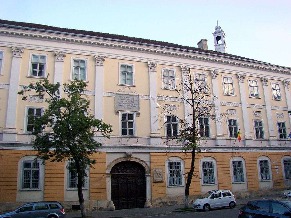 Fațada galbenă a fostului Liceu al Piariștilor din Cluj-Napoca, cu portal masiv din lemn și turn cu clopotniță.