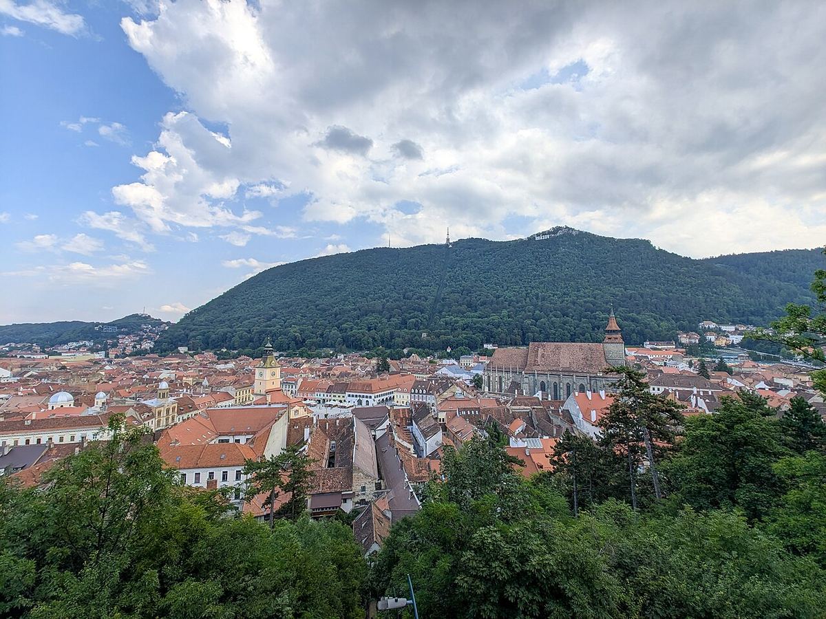Panorama orașului vechi Brașov, cu Biserica Neagră, turnul cu ceas și Muntele Tâmpa acoperit de păduri în fundal.