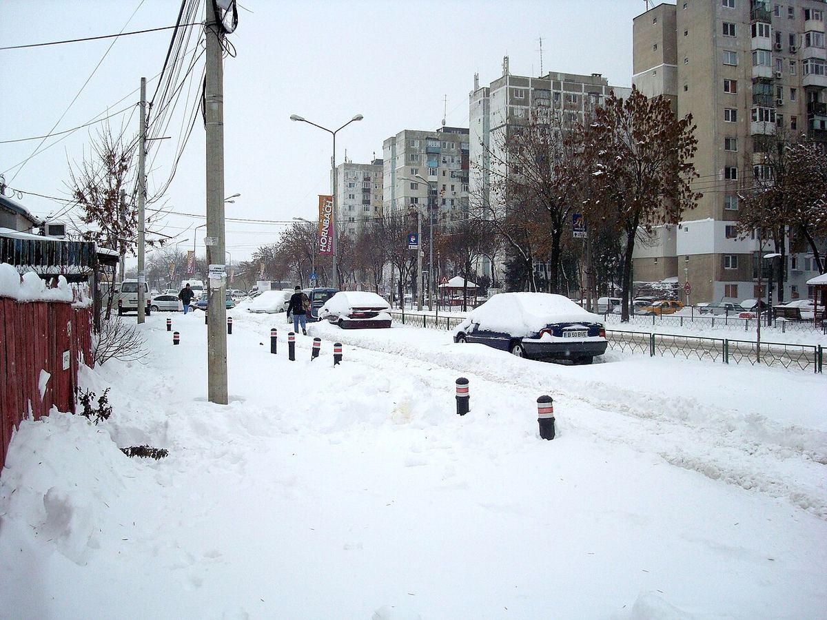 Stradă cu blocuri și mașini acoperite de zăpadă, după o ninsoare abundentă