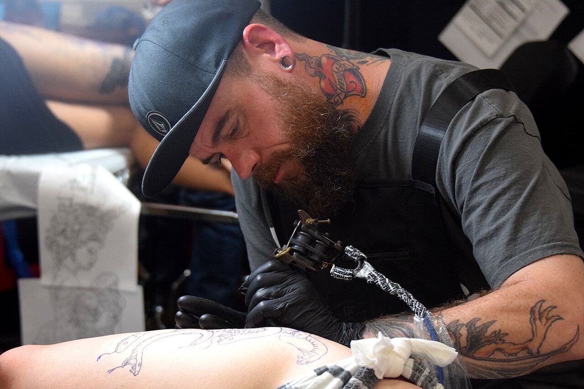 Tatuator lucrând la un desen pe brațul unui client, la un festival de tatuaje din Virginia Beach.