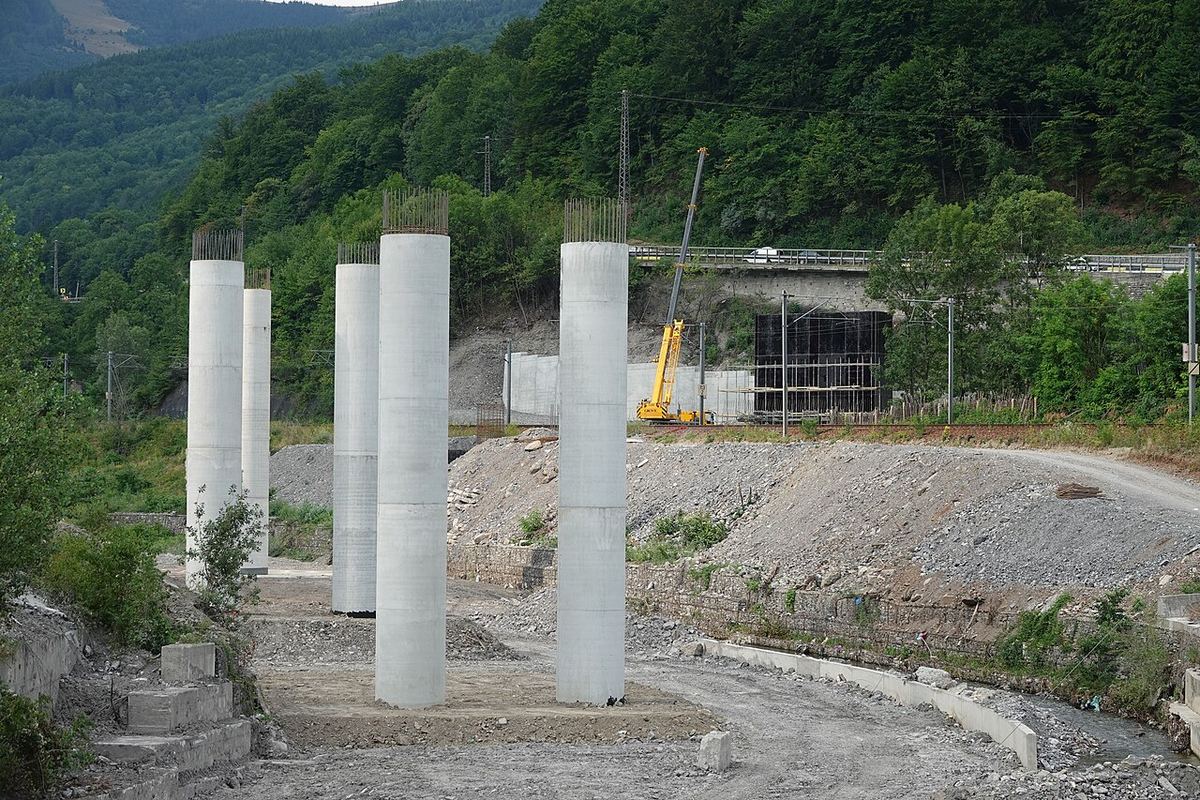 Stâlpi de beton ai unui viaduct în construcție, cu o macara galbenă în fundal, pe un șantier de centură rutieră din Prahova.