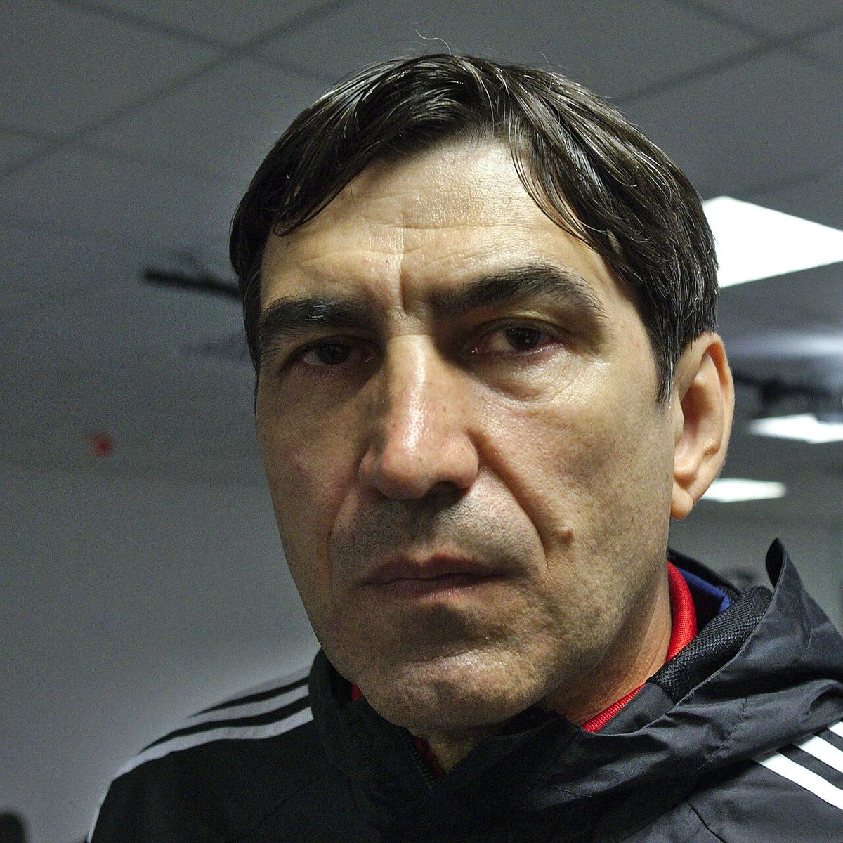 Victor Pițurcă, în prim-plan, într-un spațiu interior, purtând o geacă sport neagră cu dungi albe. Fotografie de arhivă.