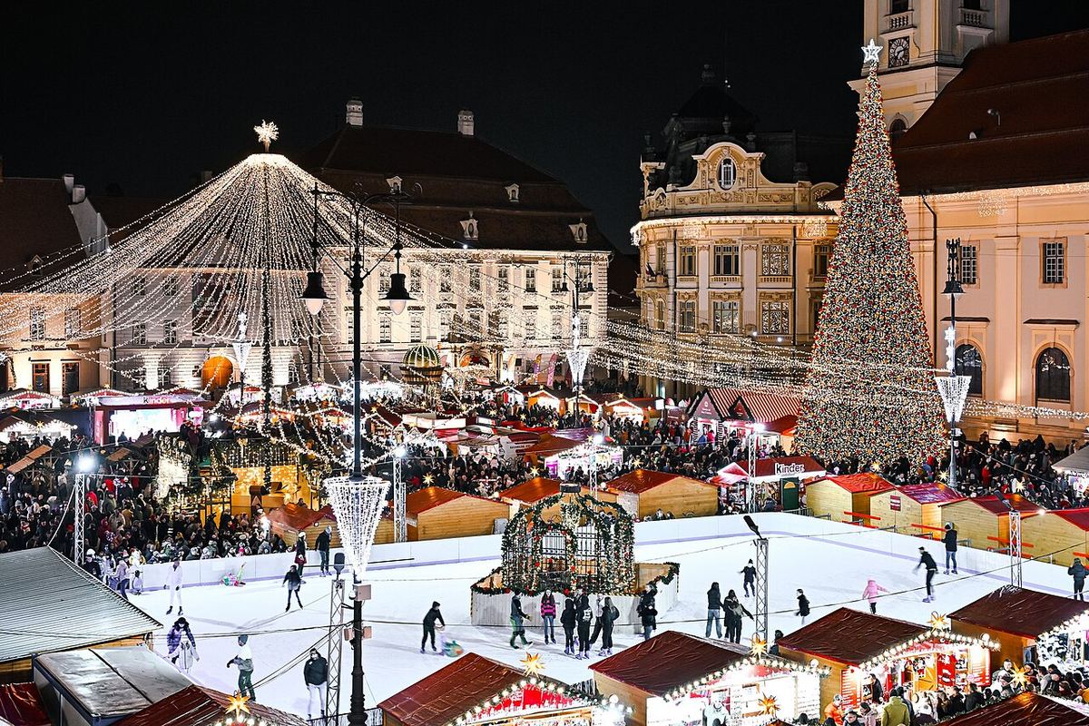 Târgul de Crăciun din Sibiu, în Piața Mare, iluminat noaptea, cu căsuțe și luminițe festive.