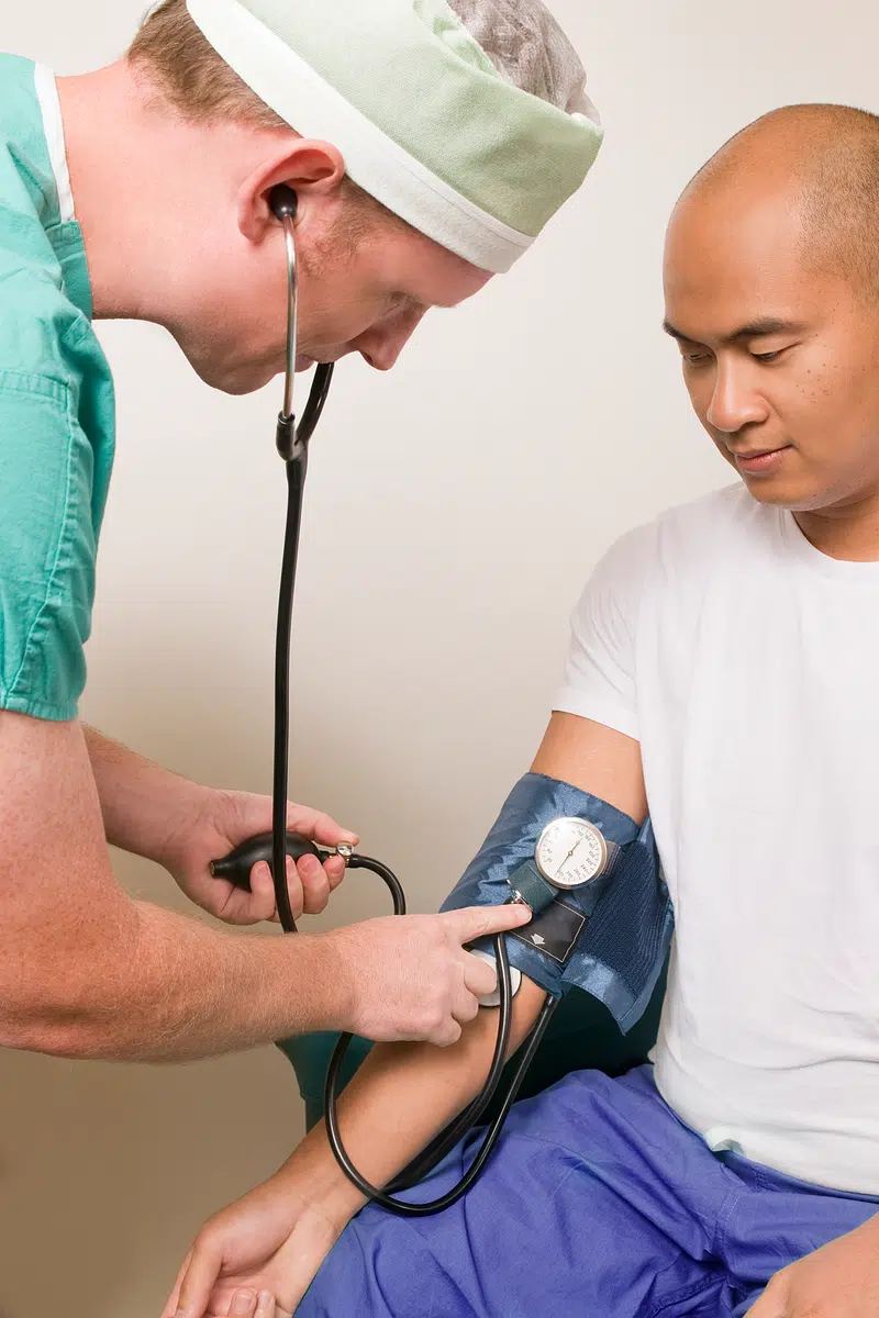 Un clinician efectuează un examen al tensiunii arteriale asupra unui pacient, ilustrație generică pentru norme medicale.