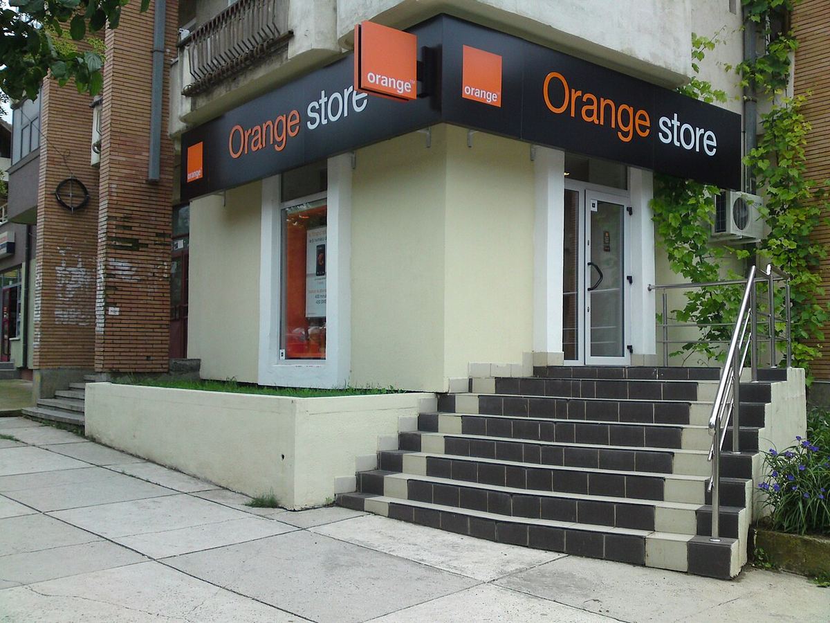 Magazinul Orange din România, cu firma portocalie pe fațada clădirii și scară cu trepte negre.