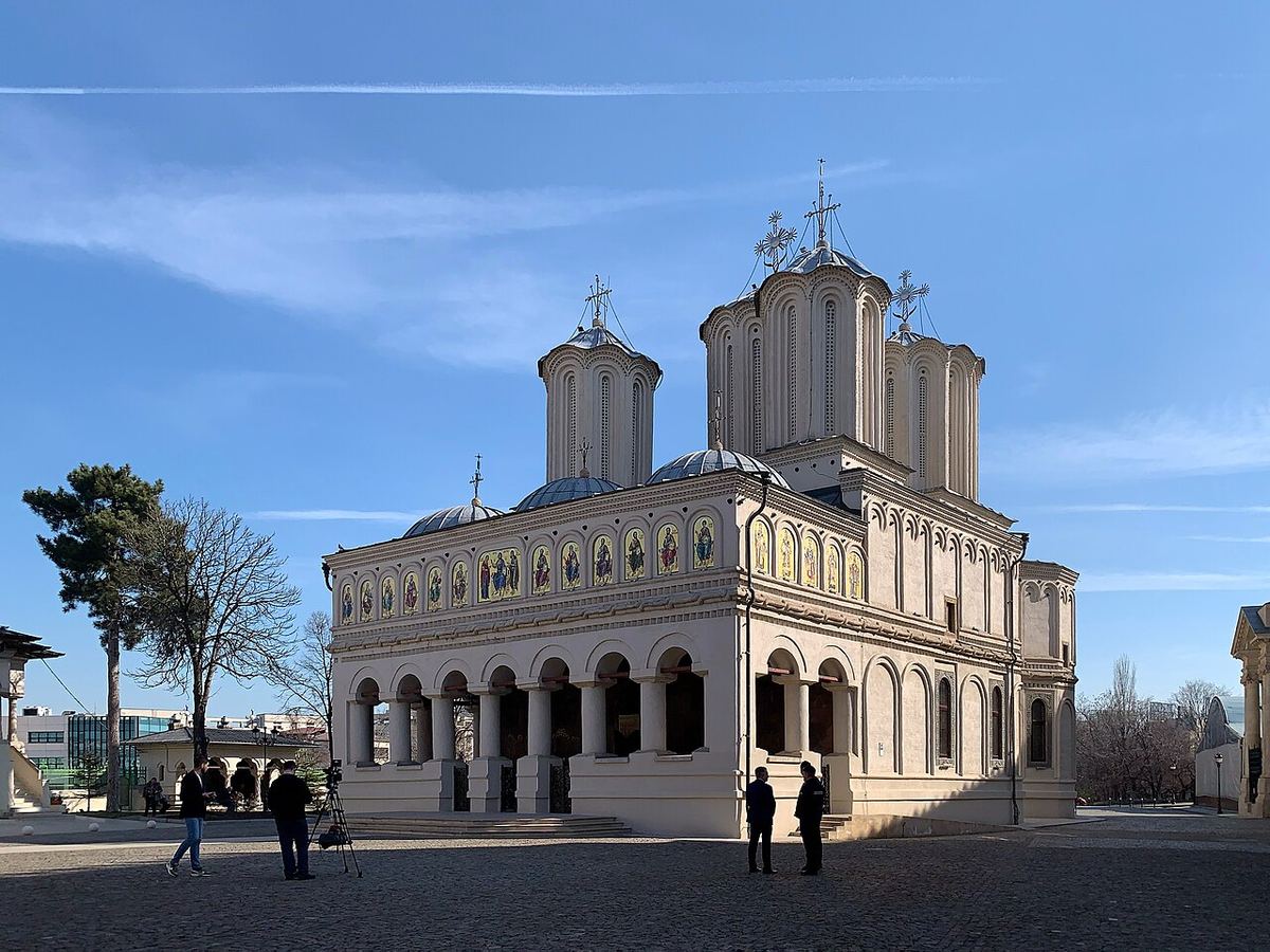 Catedrala Patriarhală din București, fotografiată ziua, cu câțiva trecători pe esplanada din fața bisericii, sub cerul senin.