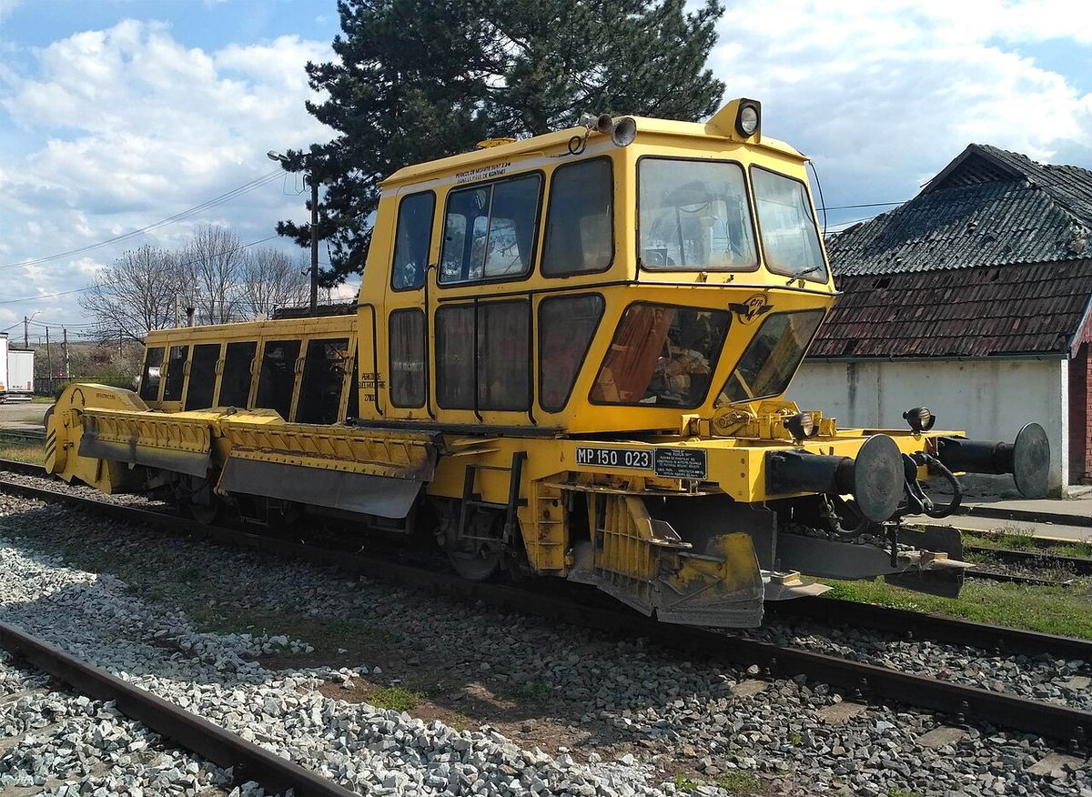 Mașină galbenă de întreținere a căii ferate (regulator de balast) pe șine, în stația Huedin, România.
