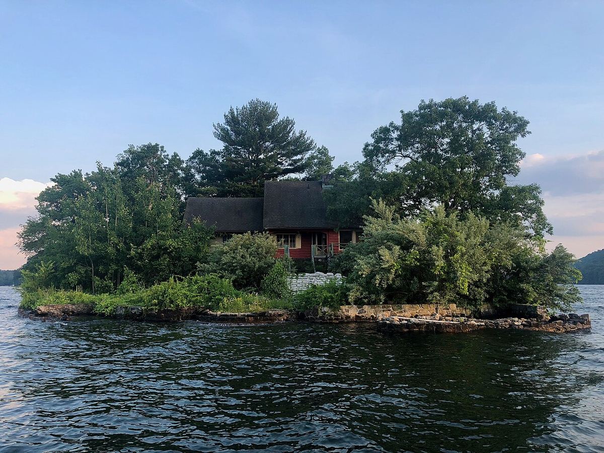 Casă mică pe o insulă dintr-un lac, fotografiată de pe malul apei, ilustrativ pentru povestea insulei din Canada.