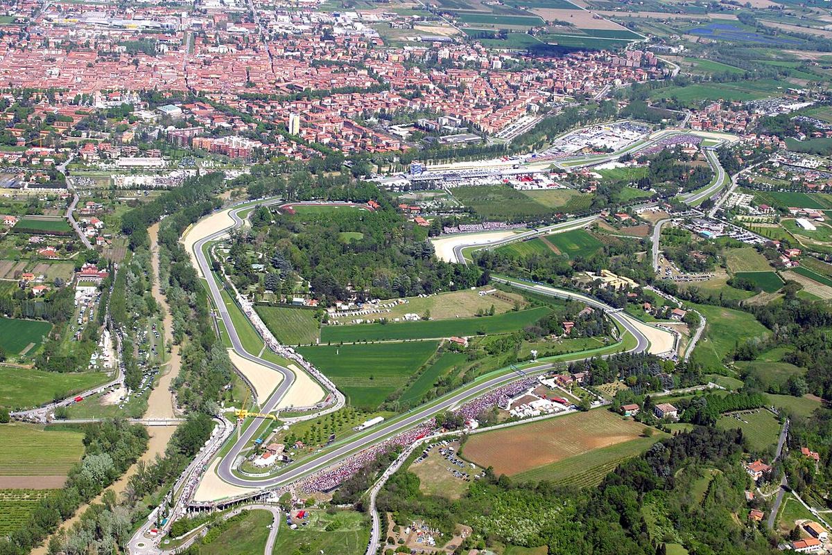 Vedere aeriană a circuitului Imola, cu tribunele și traseul de Formula 1 în prim-plan și orașul în fundal.