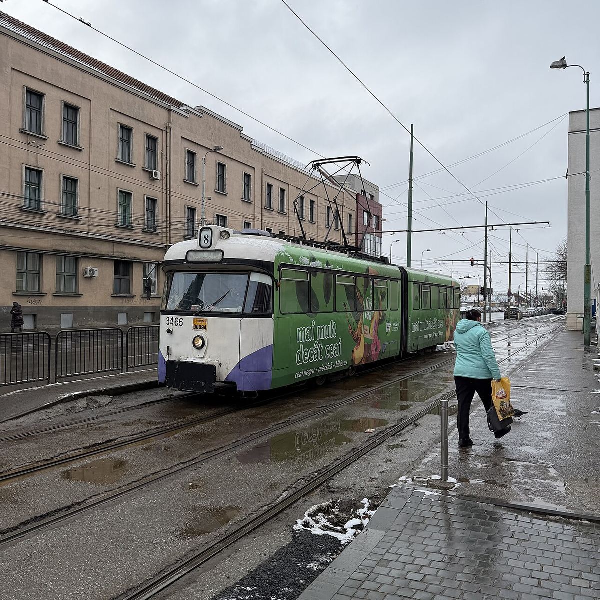 Stație de tramvai în Timișoara, fotografiată ziua, cu linii de tramvai și peroane pentru călători.