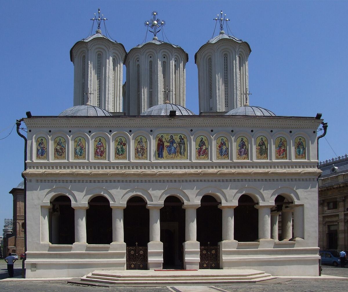 Fațada Catedralei Patriarhale din București, biserică ortodoxă cu turle albe și icoane pe perete (imagine ilustrativă).