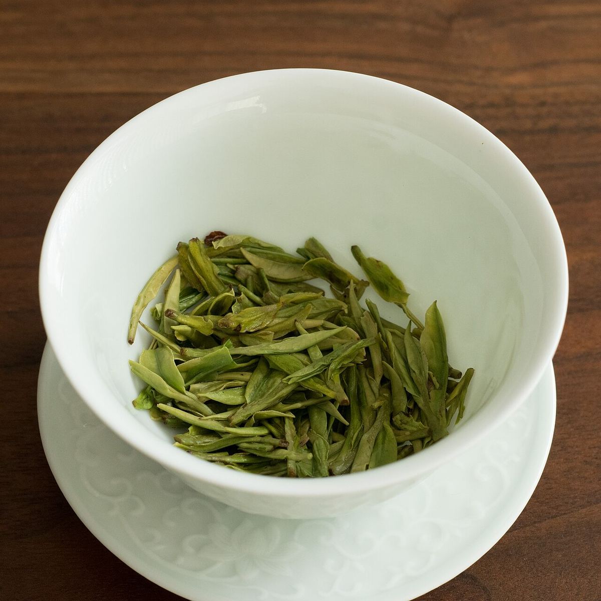 Ceai verde Longjing după prima infuzare, într-un bol gaiwan verde pal, cu frunze întinse în apă fierbinte.