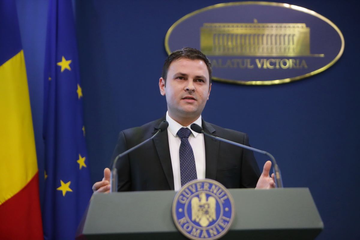 Daniel Suciu vorbind la un briefing de presă, în fața unui pupitru cu sigla Guvernului României, sub un logo Palatul Victoria.