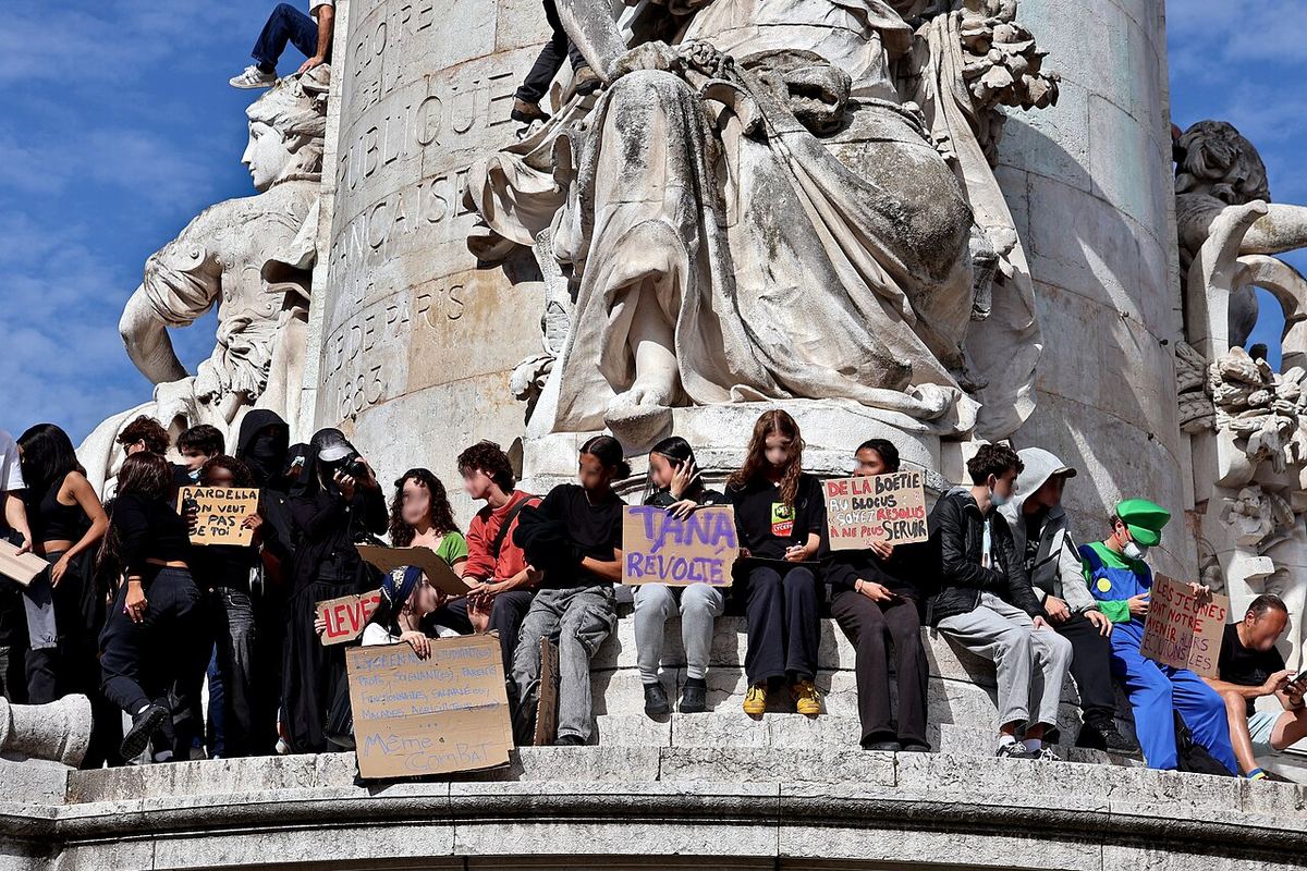 Elevi așezați pe un monument din Paris, ținând pancarte în timpul unei manifestații pentru educație.