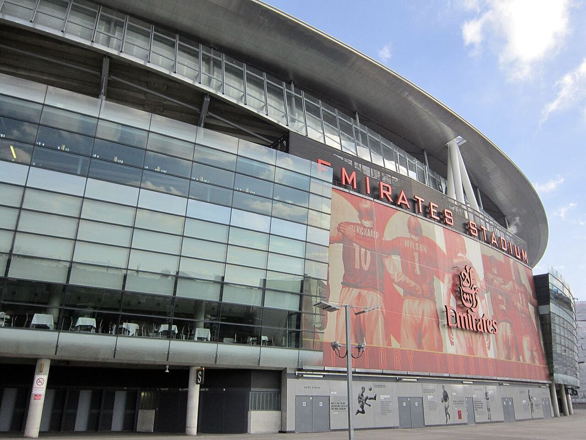 Exteriorul Stadionului Emirates, arena clubului Arsenal din Londra, cu un banner mare roșu și alb pe fațada laterală.
