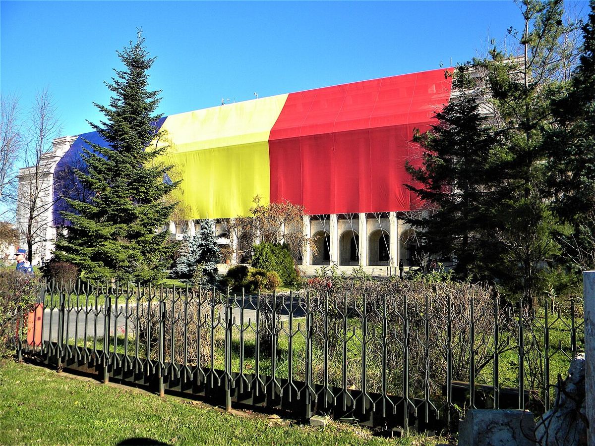 Palatul Victoria din București, sediul Guvernului României, cu o fațadă acoperită de un steag tricolor, fotografiat ziua.