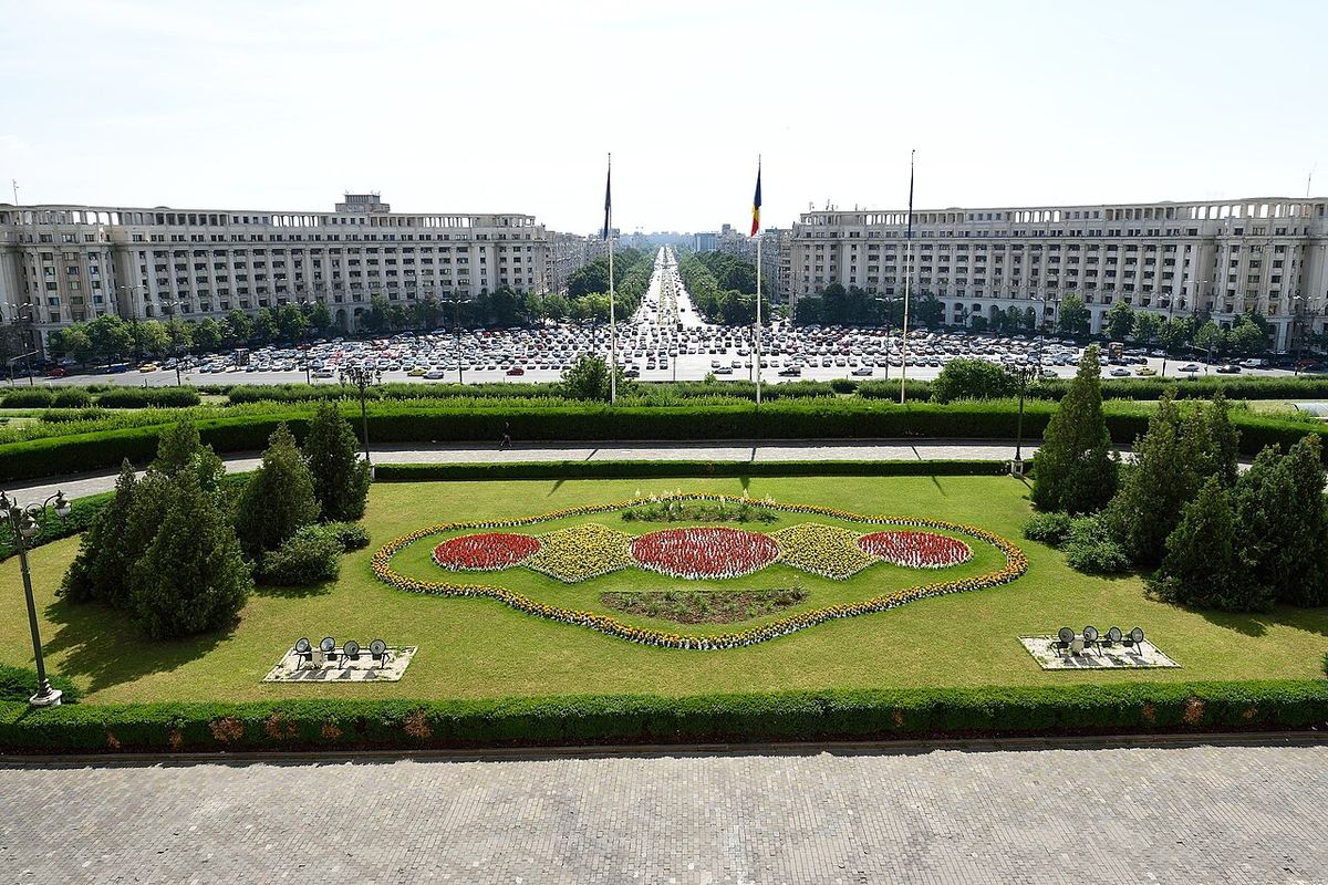 Vedere de sus a Palatului Parlamentului din București, cu grădina centrală cu flori și bulevardul din fața clădirii.
