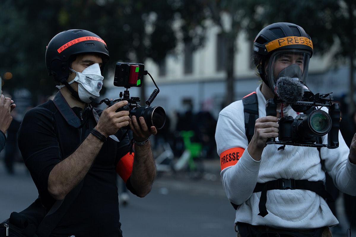 Manifestanți în fum de gaze lacrimogene, lângă vehicule și biciclete incendiate pe o stradă urbană.
