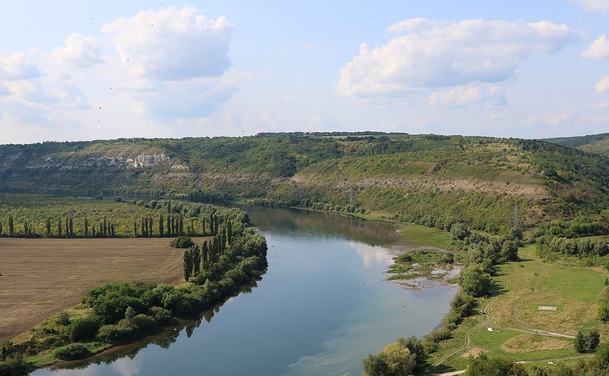 Fluviul Nistru, văzut printre dealuri împădurite, cu terenuri agricole și vegetație de-a lungul malurilor.